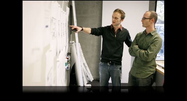 Two men standing at a board discussing.