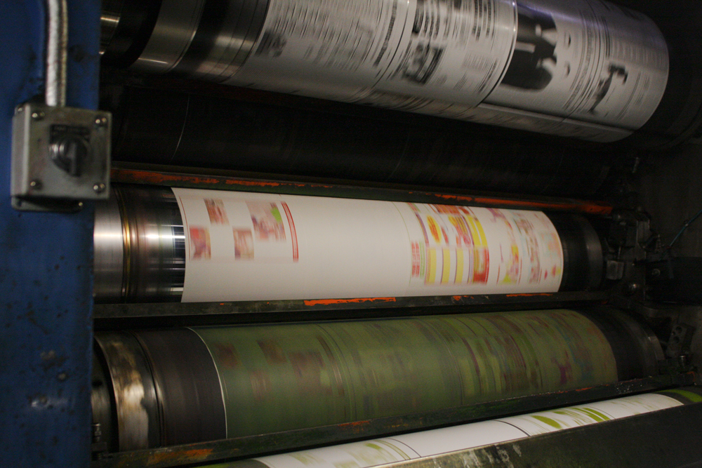 Pages of newspaper are shown flowing through a printing press.