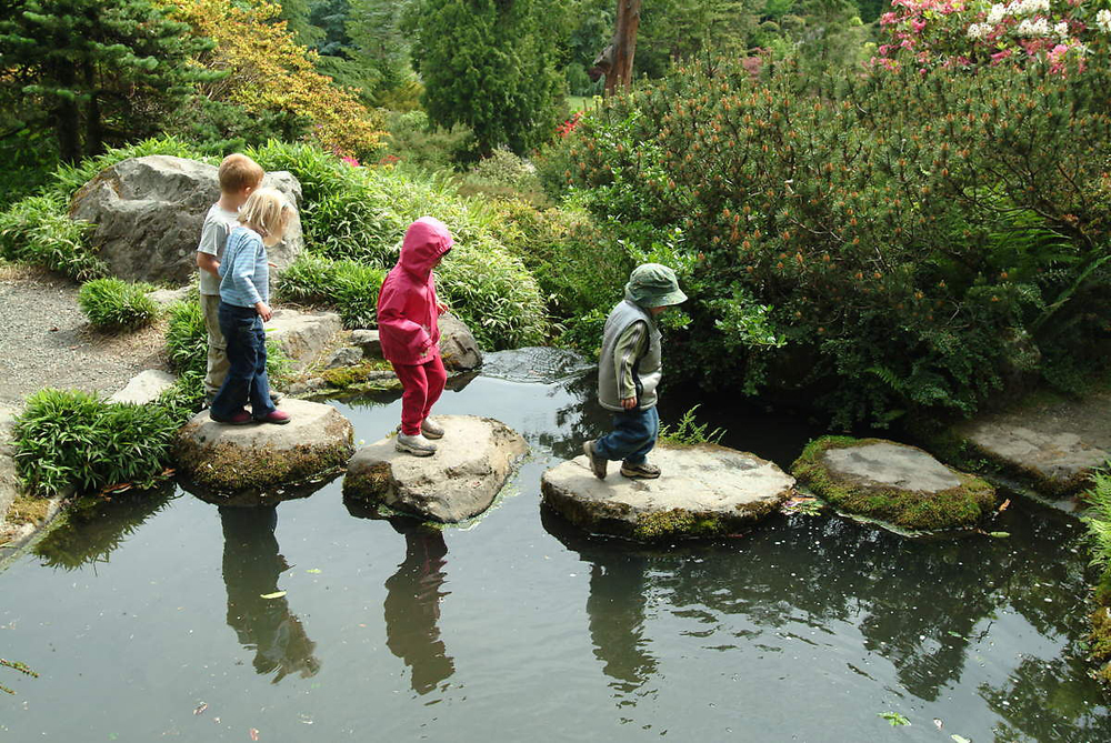 Four children are shown crossing a stream by walking on stones.