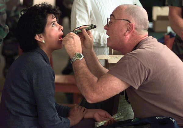 This photograph shows a dentist looking into a woman’s mouth.