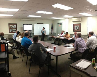 A photograph shows a group of people seated around tables in a meeting room.