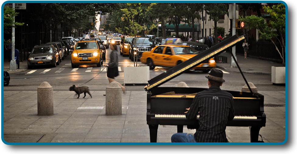 A photograph shows a person playing a piano on the sidewalk near a busy intersection in a city.