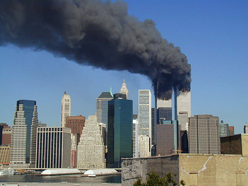 A photograph shows the World Trade Center buildings, shortly after two planes were flown into them on the morning of September 11, 2001.  Thick, black clouds of smoke stream from both buildings.