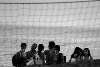 Several people are congregated by the beach. There is a net in the background.