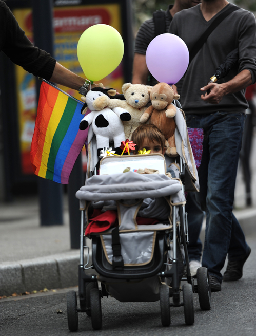 (b) shows a child in a stroller being pushed by two men.