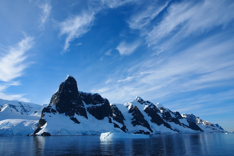 Picture of Antartica showing water, mountain, and iceberg peaks under a bright blue sky