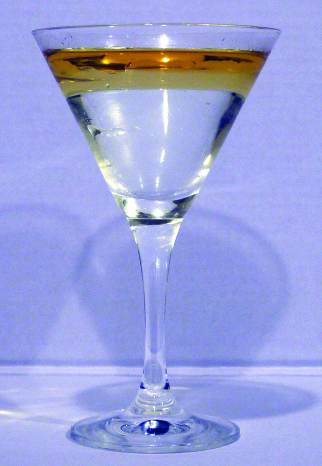 This is a photo of a clear, colorless martini glass containing a golden colored liquid layer resting on top of a clear, colorless liquid.