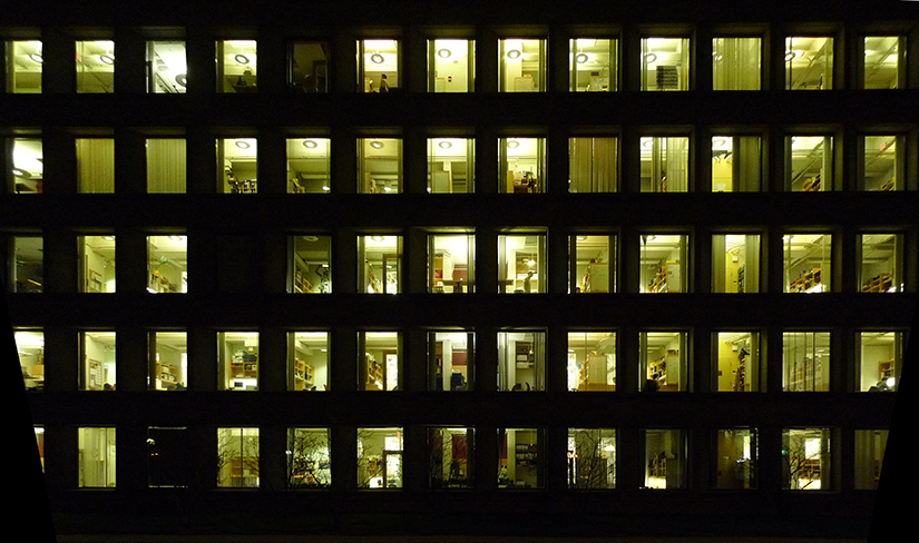  A photo of a large office building at night where you can see many people working inside after hours