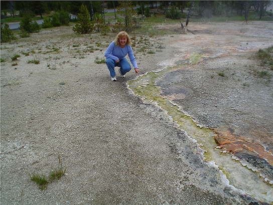 This photo shows a woman squatting next to a stream of green-colored water.