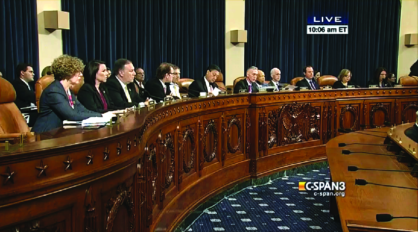 An image of several people seated behind a long wooden bench.