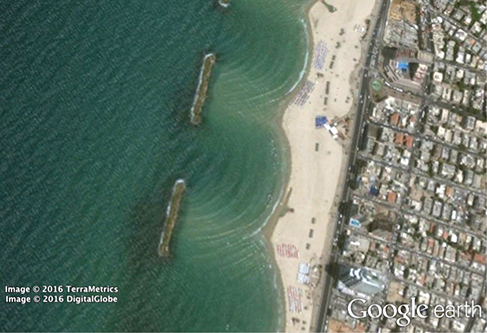 Photograph showing the top view of a breakwater near a beach. There is an opening in the breakwater allowing waves to enter.