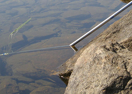 A photo shows a pole being placed in water. The pole looks like it bends where it hits the water.